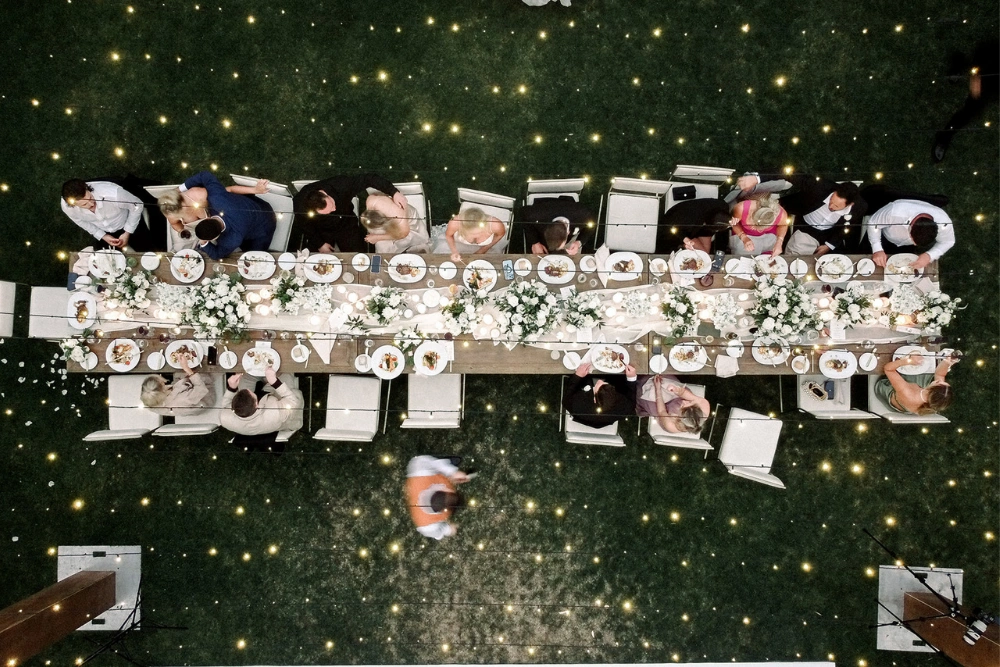 Rancho Valencia wedding lighting with overhead view of long dining table and twinkle lights across lawn